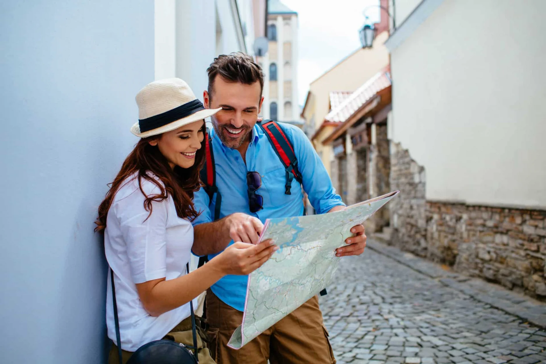 A couple studies a map together in a cobblestone street, surrounded by historic buildings, while dressed casually for an outing.